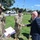 Acting SecAF Roth visits Joint Base Andrews A civilian in a blue suit is shaking hands with a uniformed military soldier in OCP (Operational Camouflage Pattern) fatigues outdoors on a grassy area. Several other soldiers in similar combat uniforms are present, one holding documents with highlighted text. A police vehicle (Dodge Durango) is visible in the background near what appears to be a secured facility entrance.