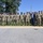 Acting SecAF Roth visits Joint Base Andrews A large group of approximately 20 military personnel in camouflage uniforms pose for a formal group photograph outdoors. One civilian in a blue suit stands among them, suggesting an official visit or ceremony. The setting appears to be near a government or municipal building on a clear, sunny day.