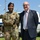 Acting SecAF Roth visits Joint Base Andrews Two individuals pose together outdoors on a sunny day. One person is wearing U.S. Air Force military uniform with multicam camouflage pattern, tactical vest, black beret, and visible name tape reading 'WILLIAMS.' The other individual is a civilian man wearing a dark pinstripe suit with a striped shirt and tie.