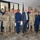 Acting SecAF Roth visits Joint Base Andrews A group photo featuring approximately 13 individuals, mostly in military uniforms, posing together indoors. One civilian man wearing a blue pinstripe suit and glasses stands at the center of the group. The setting appears to be a military facility or event room with an American flag and a POW/MIA flag visible in the background.