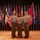 Three U.S. Marine Corps personnel in service uniforms (Charlie or Alpha service uniform) pose together on a wooden stage in front of a large display of U.S. state flags and military flags. The setting appears to be a formal military ceremony or official event, likely a change of command, promotion, or retirement ceremony. All three individuals are smiling and wearing ribbons and decorations on their uniforms.