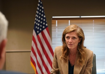 A formal meeting is taking place in what appears to be a government office setting. A nameplate on the table identifies the seated individual as 'Samantha Power, Administrator, USAID.' An American flag and a USAID organizational flag are visible in the background.