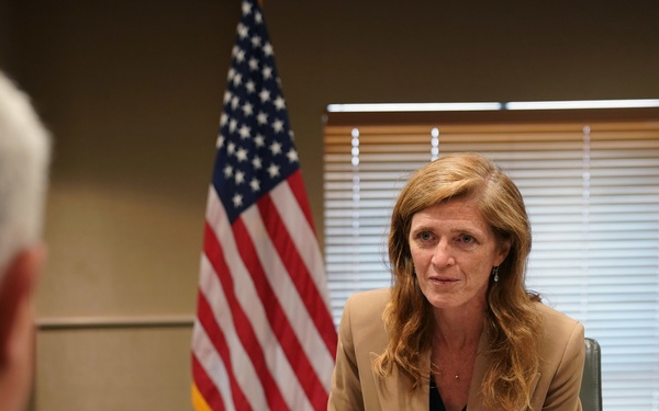 A formal meeting is taking place in what appears to be a government office setting. A nameplate on the table identifies the seated individual as 'Samantha Power, Administrator, USAID.' An American flag and a USAID organizational flag are visible in the background.