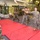 A group of U.S. Marines in digital camouflage uniforms are conducting close-combat or martial arts training inside what appears to be the well deck or cargo bay of a naval vessel. An instructor on the left is demonstrating stick/pugil fighting techniques to several trainees who are practicing with wooden or padded training sticks. Red training mats are laid out on the deck floor to provide a designated training area.