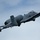 A U.S. Air Force A-10 Thunderbolt II (Warthog) attack aircraft is captured in flight against an overcast sky. The aircraft is in a slight bank maneuver, displaying its distinctive twin-engine rear-mounted configuration and straight wings. Tail markings indicate 'DM' (Davis-Monthan Air Force Base) with a partial serial number visible as '240'.