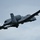 A U.S. Air Force A-10 Thunderbolt II (Warthog) attack aircraft is captured in flight against an overcast gray sky. The aircraft is banking at an angle, providing a clear view of its underside and twin tail configuration. Tail markings indicate 'DM' code and partial serial number '240', consistent with Davis-Monthan Air Force Base assignment.