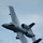 A U.S. Air Force A-10 Thunderbolt II (Warthog) attack aircraft is captured in a steep banking maneuver against an overcast sky. The aircraft is in a near-vertical roll, showcasing its distinctive twin-engine rear-mounted configuration and straight wings. Vapor condensation trails are visible streaming off the fuselage, indicating high-speed low-altitude flight.