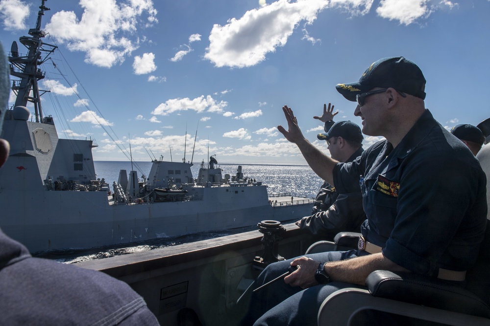 Cmdr. J.J. Murawski (front), commanding officer and Cmdr. Charles Cooper (back), executive officer wave to the crew of the HMAS Brisbane (FFH 41) as they sail alongside aboard USS Rafael Peralta (DDG 115) during Exercise Talisman Sabre 21
