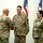 A military ceremony is taking place in an indoor setting where a senior officer is shaking hands with a soldier named Locker from Ohio. Two soldiers are standing at attention while another officer observes seated in the background. The scene appears to be an awards, promotion, or recognition ceremony.