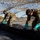 Talisman Sabre 21: U.S., Australian forces perform bilateral fuel training Several personnel wearing camouflage uniforms and teal/green protective gloves are working together to lay or spread a large black tarpaulin or geotextile fabric on the ground. They are operating beneath a large camouflage netting canopy that provides overhead cover. The scene appears to be a military or field engineering operation in an outdoor, sandy environment.