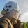 Talisman Sabre 21: U.S., Australian forces perform bilateral fuel training A close-up photograph of one or two firefighters wearing white protective helmets with clear face shields, covered in water droplets. They are dressed in tan/brown firefighting turnout gear with high-visibility yellow-green reflective striping. Smoke or steam is visible in the background, suggesting an active firefighting or training scenario.