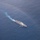 USS Sioux City Transits the Caribbean Sea An aerial photograph of a gray naval warship underway in open blue ocean waters. The vessel appears to be a modern littoral combat ship or similar fast surface combatant, leaving a white wake trail behind it. A partial rainbow is visible in the upper portion of the image, and a faint discoloration of the water is visible around the ship.