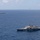 HSC 28 Helicopter Takes Off from the Flight Deck The image shows two U.S. Navy Littoral Combat Ships (LCS) operating in open blue ocean waters under partly cloudy skies. A helicopter is visible in the upper right portion of the image, appearing to conduct flight operations near the vessels. The foreground ship displays the distinctive trimaran or monohull design characteristic of the Freedom or Independence-class LCS.