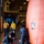 Military personnel, likely U.S. Navy sailors, are working inside what appears to be a ship's hangar bay or vehicle deck. They are inflating or setting up a large orange inflatable structure, possibly a damage control or training device, using a red blower/fan unit connected by hoses. Several personnel in yellow jerseys and face masks observe the operation.