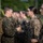The image shows a group of female military personnel in camouflage uniforms during what appears to be a formal inspection or administrative activity. One service member is presenting or reviewing a document/card with another who is wearing glasses and a bun hairstyle. Multiple personnel are visible in formation in the background.