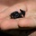 A small black beetle is resting on the palm of a human hand. The insect appears to be a dung beetle or similar scarab-type beetle, dark in color with visible segmentation and legs. The hand is slightly dirty or dusty, suggesting an outdoor setting.