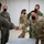 Combat aircraft integrate in Hawaii for exercise Sentry Aloha-21 Military personnel in a indoor facility are greeting each other with a fist bump while wearing face masks, consistent with COVID-19 era protocols. The group includes individuals in both OCP (Operational Camouflage Pattern) uniforms and olive green flight suits. An American flag patch is visible on one service member's sleeve, indicating U.S. military affiliation.