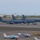 Combat aircraft integrate in Hawaii for exercise Sentry Aloha-21 The image shows a mixed-use airport ramp with two large U.S. Air Force KC-135 Stratotanker aircraft parked in the background alongside what appears to be a third military aircraft. In the foreground, several small general aviation aircraft are parked on the tarmac, including identifiable tail numbers N888PE, N2T (partially visible), and N2491E. The setting appears to be a joint-use civilian and military airfield, likely in Hawaii based on the terrain and vegetation.