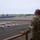 Combat aircraft integrate in Hawaii for exercise Sentry Aloha-21 A U.S. Air Force service member in OCP (Operational Camouflage Pattern) uniform stands on an elevated observation deck overlooking a flight line or tarmac. The ramp area contains a mix of large military aircraft, likely KC-135 tankers, alongside several small civilian general aviation aircraft. The setting appears to be a joint-use military and civilian airfield.