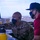 Combat aircraft integrate in Hawaii for exercise Sentry Aloha-21 Two individuals are working together in what appears to be a military air traffic control tower. One person is wearing a U.S. Air Force uniform with the name tape 'ALEJO' visible, while the other is in civilian attire (red polo shirt and dark baseball cap). Both are wearing black face masks and communication earpieces, suggesting this was taken during the COVID-19 pandemic period.