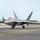 Combat aircraft integrate in Hawaii for exercise Sentry Aloha-21 A U.S. Air Force F-22 Raptor stealth fighter jet is taxiing on a runway, identifiable by the 'HH' tail code indicating assignment to Hickam Air Force Base (Joint Base Pearl Harbor-Hickam) in Hawaii. The aircraft is on the ground with landing gear deployed, moving along a marked taxiway. The surrounding environment features tropical vegetation, military infrastructure, and a partly cloudy sky consistent with a Hawaiian setting.