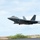 Combat aircraft integrate in Hawaii for exercise Sentry Aloha-21 A U.S. Air Force F-22 Raptor stealth fighter jet is captured during takeoff or low-altitude flight just above a runway. The aircraft bears the tail code 'HH', indicating assignment to Hickam Air Force Base (now Joint Base Pearl Harbor-Hickam) in Hawaii. Motion blur in the background suggests high speed and dynamic camera panning technique.