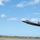 Combat aircraft integrate in Hawaii for exercise Sentry Aloha-21 A U.S. Air Force F-22 Raptor stealth fighter jet is captured in low-altitude flight, appearing to be taking off or performing a low pass over a runway. The aircraft displays tail code 'HH' on its twin vertical stabilizers, indicating assignment to the 15th Wing at Joint Base Pearl Harbor-Hickam, Hawaii. The image uses a panning technique, creating motion blur in the background while keeping the aircraft relatively sharp.