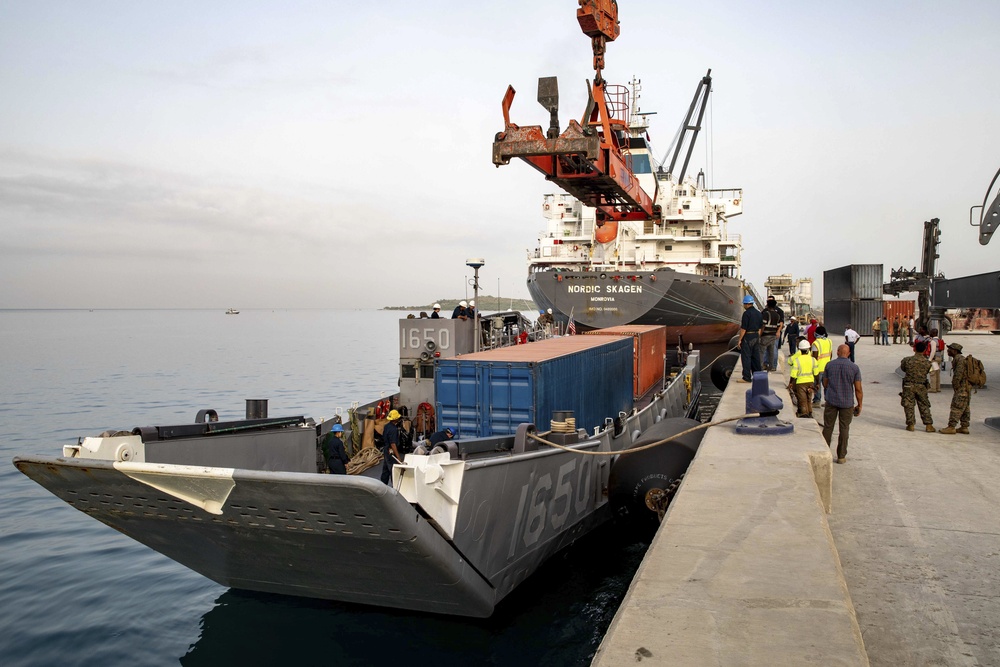 Shipping Containers Of Humanitarian Aid Are Loaded Onto A U.S. Navy LCU