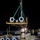 U.S. Navy Seabees assigned to NMCB-5 support the Defense Logistics Agency A nighttime military logistics operation on what appears to be a dock or pier, where personnel in military uniforms are managing a crane lift of large pipe sections or flanged cylindrical components. A central figure wearing a hard hat and camouflage uniform holds a tag line (guide rope) to control the suspended load. At least three personnel are visible coordinating the lift operation.