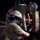 U.S. Navy Seabees assigned to NMCB-5 support the Defense Logistics Agency Two military personnel wearing hard hats and face masks are working together on a piece of heavily rusted metal infrastructure during nighttime operations. Both individuals are wearing olive/tan t-shirts and appear to be engaged in maintenance or salvage work. The foreground worker is in U.S. Navy digital camouflage (NWU) trousers, suggesting U.S. Navy affiliation.