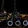 U.S. Navy Seabees assigned to NMCB-5 support the Defense Logistics Agency Military personnel, appearing to be U.S. Navy Seabees or similar construction/engineering unit, are conducting a nighttime operation handling large black flanged pipe sections on what appears to be a dock or pier. A crane with green rigging straps is being used to lift or position the heavy pipe sections. The operation involves multiple personnel working in coordination, with at least one wearing a hard hat and others in standard military working uniforms.