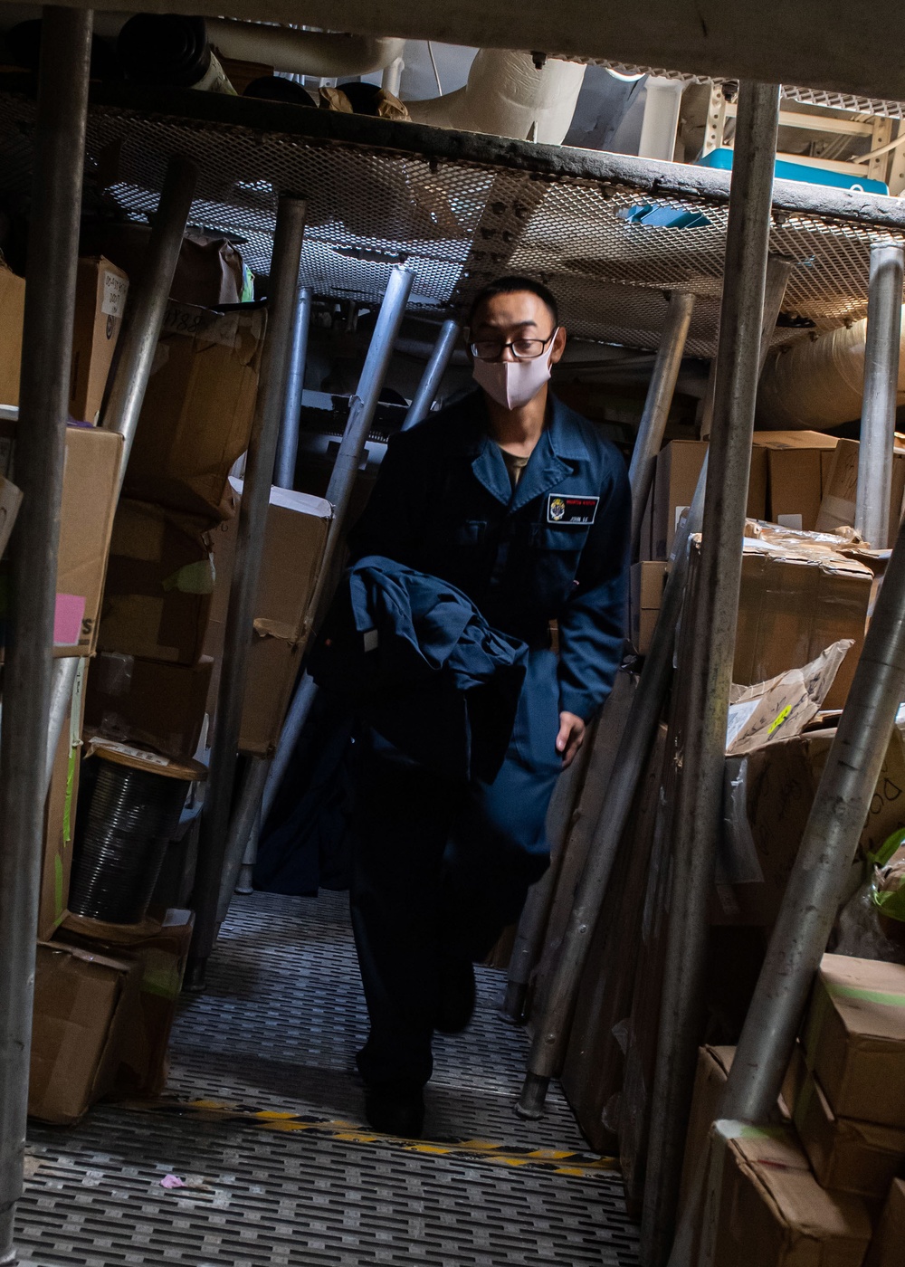 USS Mustin Sailor Retrieves Coveralls in a Storage Space