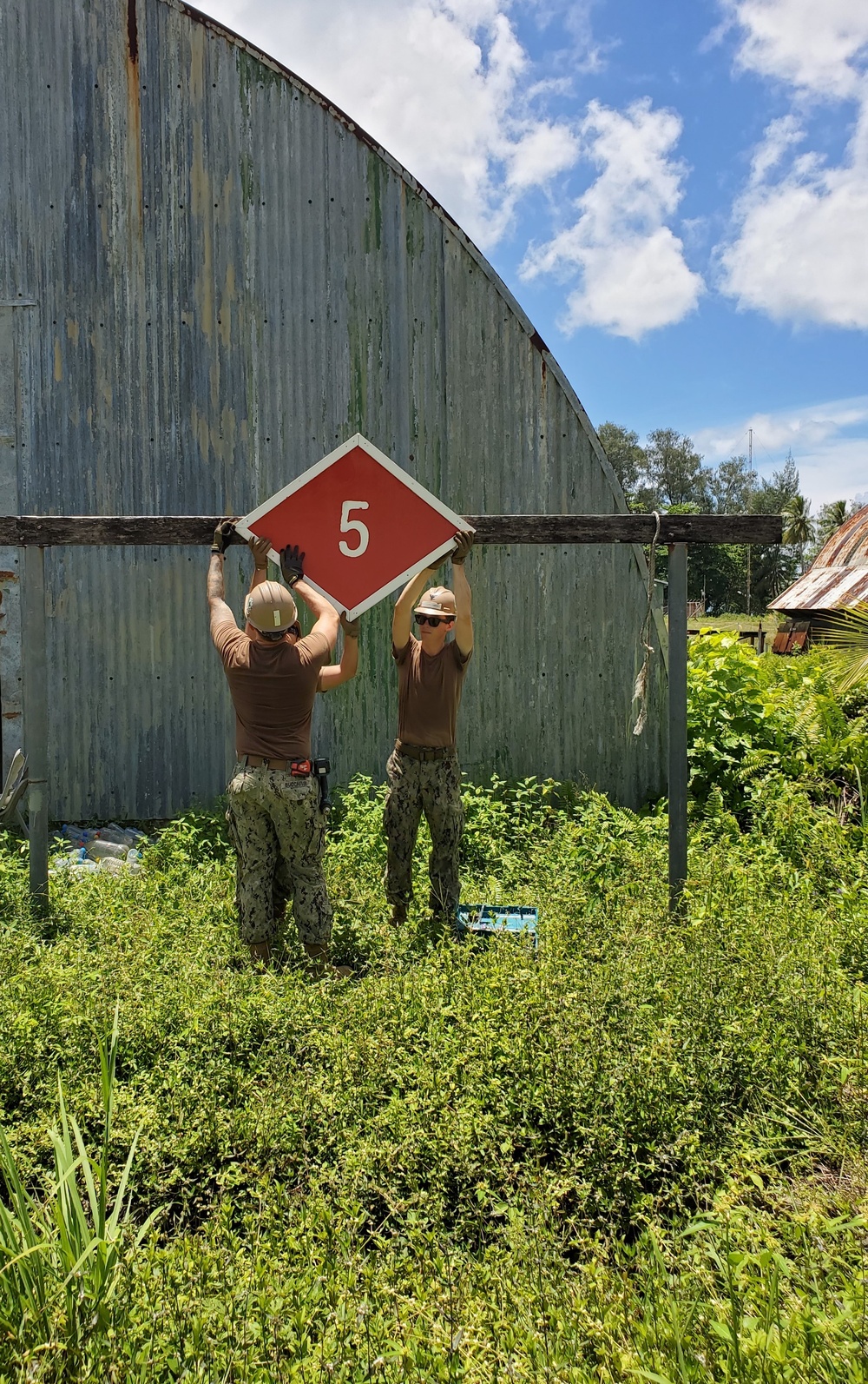 U.S. Navy Seabees assigned to NMCB-5 hang a battalion evaluation equipment program sign