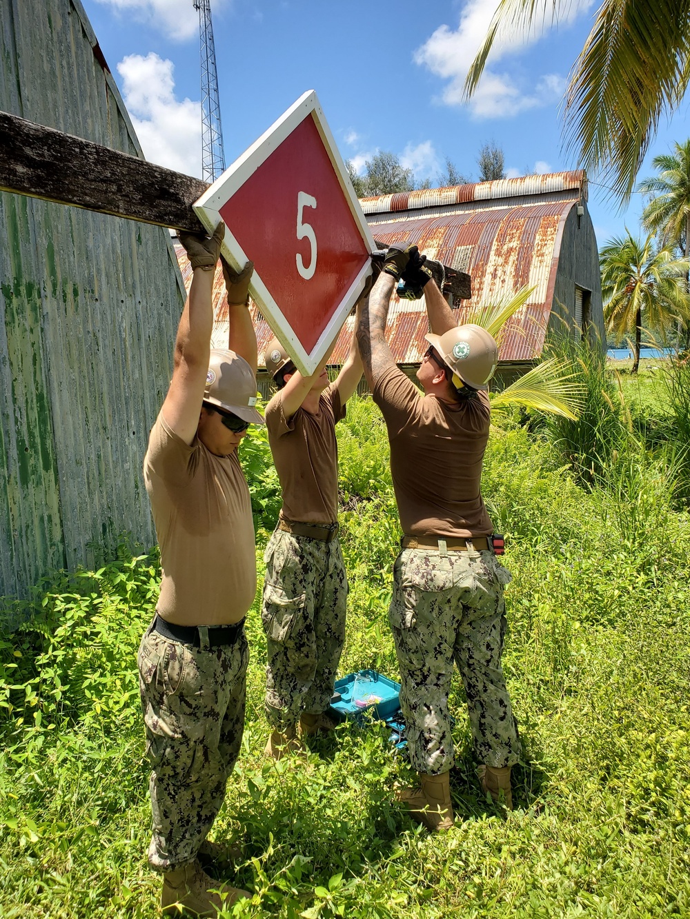 U.S. Navy Seabees assigned to NMCB-5 hang a battalion evaluation equipment program sign
