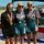 Navy Sweeps Men and Women Team Golds at 2021 Armed Forces Triathlon Three women pose together on what appears to be a podium at an outdoor athletic competition, all wearing medals around their necks. Two of the women are wearing matching teal Navy triathlon/cycling uniforms, while the third wears a black jacket with a Marine Corps emblem. The setting appears to be a military sports competition near a body of water with hills in the background.