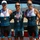 Navy Sweeps Men and Women Team Golds at 2021 Armed Forces Triathlon Three male athletes pose together at what appears to be a military triathlon competition, each wearing medals around their necks. The center athlete wears a Navy triathlon suit, while the two flanking athletes wear U.S. Air Force triathlon uniforms. The setting appears to be an outdoor awards ceremony near a body of water with mountains in the background.