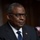 SECDEF, CJCS, CENTCOM Senate Armed Services Testimony A man in formal attire is seated at what appears to be an official hearing or formal proceeding, positioned in front of a microphone. He is wearing a dark suit with a blue tie and has a small American flag pin on his lapel. The setting and composition suggest a formal governmental or institutional environment.