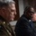 SECDEF, CJCS, CENTCOM Senate Armed Services Testimony The image shows three individuals seated at what appears to be a formal hearing or official proceeding. The central figure in focus is wearing a dark suit with a blue tie and black-framed glasses. To the left, partially out of focus, is a person in military dress uniform with visible insignia.