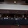 SECDEF, CJCS, CENTCOM Senate Armed Services Testimony A formal congressional hearing or testimony session featuring senior U.S. military and defense officials seated at a long draped table. Name placards visible identify GEN Milley (left), Sec. Austin (center), and Gen. McKenzie (right). The setting appears to be a formal government hearing room with recessed lighting, a wall clock, and EXIT signs visible.