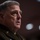 SECDEF, CJCS, CENTCOM Senate Armed Services Testimony A senior U.S. Army officer in dress uniform is speaking, likely at a congressional hearing or formal testimony setting. The subject is wearing a green Army service uniform with multiple visible insignia and patches. The background is blurred with bokeh lighting effects, suggesting a formal indoor setting.