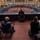 SECDEF, CJCS, CENTCOM Senate Armed Services Testimony A formal congressional hearing is taking place in what appears to be a U.S. Senate committee room, with a large horseshoe-shaped dais where senators are seated facing witnesses. Audience members and military personnel are seated in the foreground, socially distanced, with some wearing face masks suggesting this occurred during the COVID-19 pandemic period. Name placards visible on the witness table include 'Gen. McKenzie' and 'GEN Milley', indicating a military-related hearing.