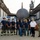 Firefighters Tour Submarine A group of approximately 12 personnel, including firefighters and a Navy sailor, pose for a group photo in front of a submarine in what appears to be a dry dock or shipyard facility. The firefighters are wearing helmets with visible numbers (51, 52, 53, 55) and face masks, alongside a person in a white uniform shirt and a Navy sailor in camouflage utilities. The large dark hull of a submarine dominates the background between industrial dry dock structures.