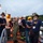 Firefighters Tour Submarine A group of firefighters and emergency personnel, along with a Navy sailor in camouflage uniform, are gathered on what appears to be a dock or vessel platform during dusk or early morning. The scene appears to be a briefing or coordination meeting, possibly for a training exercise or emergency response operation near a waterfront. Several personnel are wearing face masks, suggesting this was taken during the COVID-19 pandemic period.