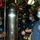 Firefighters Tour Submarine Four individuals wearing blue surgical face masks are gathered in a confined, equipment-dense space that appears to be the interior of a naval vessel or submarine. Three of the individuals are wearing navy blue fire department shirts, with one also wearing a firefighter's helmet, while a fourth wears a yellow hard hat. The group appears to be receiving a tour or briefing in the technical space.