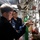 Two or more naval personnel in dark blue uniforms are conducting an inspection or maintenance check in a narrow shipboard passageway or machinery space. The foreground figure is examining equipment mounted on a wall panel, including what appears to be a fire extinguisher with an inspection tag attached. The setting is consistent with the interior of a military vessel, featuring pipes, valves, gauges, and compressed gas cylinders.
