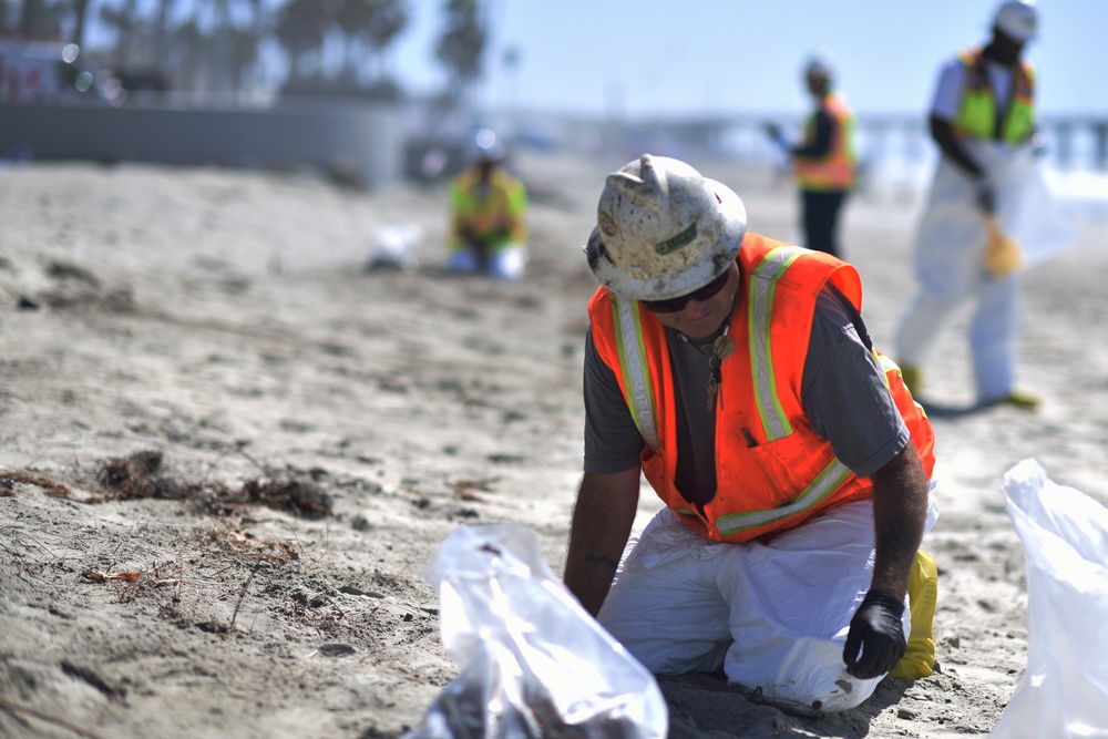 A clean up team member removes tar balls from Oceanside Harbor