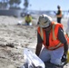 A clean up team member removes tar balls from Oceanside Harbor