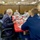 A formal meeting or briefing is taking place around a red-covered conference table, likely aboard a military vessel or in a government facility. Several participants are wearing face masks, suggesting this occurred during the COVID-19 pandemic period. The group includes uniformed military personnel and civilians engaged in discussion.