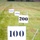 The image shows a series of distance marker signs placed at regular intervals across a grassy field or range. The signs display numbers 100, 200, 400, and 500 (partially visible), indicating measured distances in yards or meters. This appears to be a shooting range, golf driving range, or similar measured outdoor facility.