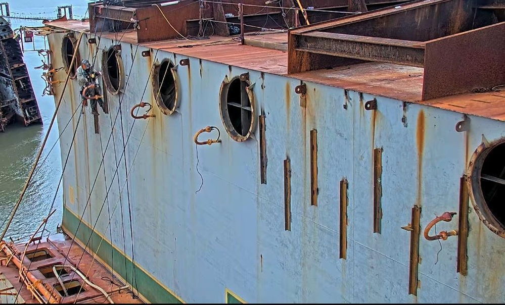 A rope-access technician welds steel reinforcement plates